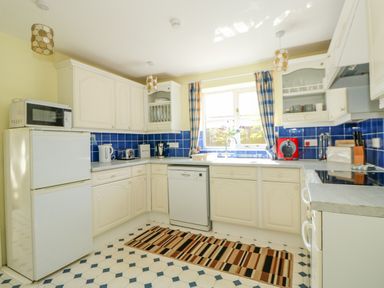 A kitchen with white cabinets blue tiled backsplash and striped rug at The Granary Cottage in Gayton near King's Lynn