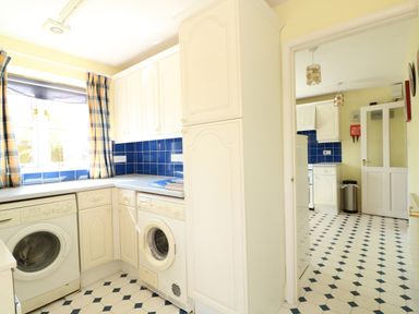 A kitchen with white cabinets blue tiled backsplash washer and dryer and checkered floor at The Granary Cottage in Gayton near King's Lynn