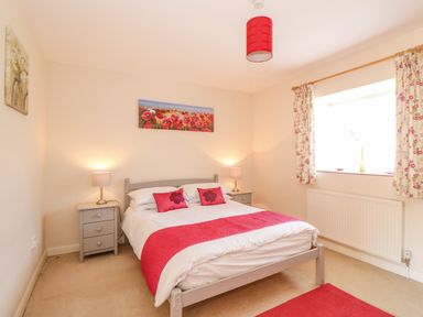 A bedroom with a double bed red accents two bedside tables lamps window with floral curtains at The Granary Cottage in Gayton near King's Lynn