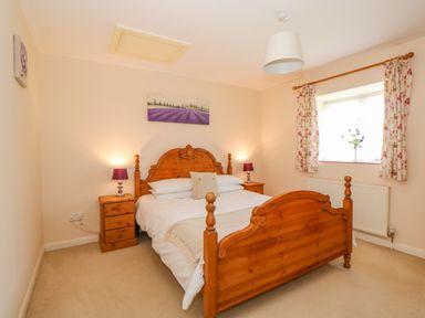 A bedroom with a wooden double bed two bedside tables with lamps a window with floral curtains and a painting above the bed at The Granary Cottage in Gayton near King's Lynn