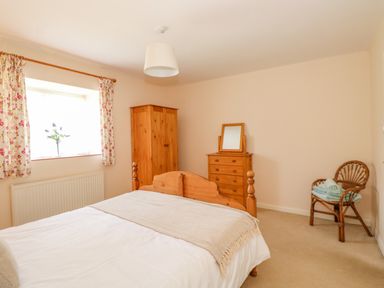 A bedroom with a wooden bed, wardrobe, chest of drawers with mirror, chair with towels, and floral curtains at The Granary Cottage in Gayton near King's Lynn
