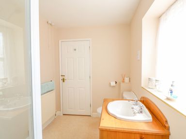 A bathroom with a sink on a wooden cabinet a toilet a window and a closed door at The Granary Cottage in Gayton near King's Lynn