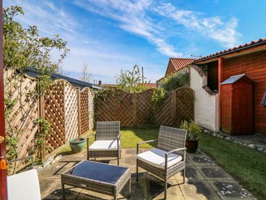 An outdoor patio area with chairs a table a wooden fence and a small shed at The Granary Cottage in Gayton near Kings Lynn