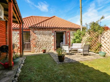 A garden with patio furniture and potted plants outside a brick and stone building with a tiled roof at The Granary Cottage in Gayton near Kings Lynn