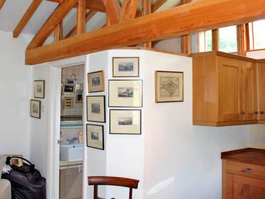 A room with wooden ceiling beams framed pictures on white walls and wooden kitchen cabinets at The Springs in Ashey near Brading and Ryde
