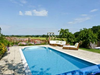 An outdoor swimming pool with stone paving and wicker sofas in a garden at The Springs in Ashey near Brading and Ryde