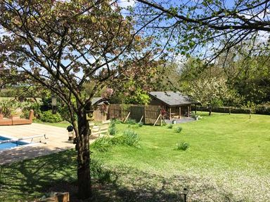 A garden with a tree and bird feeders near a swimming pool and a wooden cabin at The Springs in Ashey near Brading and Ryde