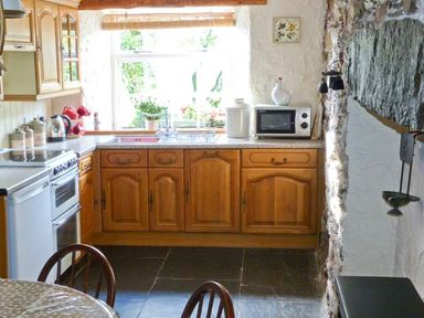 A kitchen with wooden cabinets a stove a microwave and a window at High Kiln Bank Cottage in Seathwaite Duddon Valley