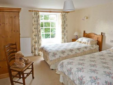 A bedroom with two single beds floral bedding wooden furniture and a window with floral curtains at High Kiln Bank Cottage Seathwaite Duddon Valley
