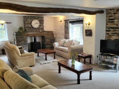 A living room with sofas a stone fireplace wooden tables a television and a vase with flowers at High Kiln Bank Cottage in Seathwaite Duddon Valley