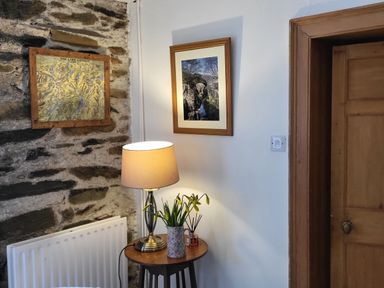 A corner with a stone wall and a white wall with a wooden door a table with a lamp flowers and a picture frame at High Kiln Bank Cottage in Seathwaite Duddon Valley