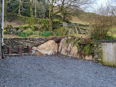 A gravel driveway with stone walls and a wooden shed surrounded by trees and plants at High Kiln Bank Cottage in Seathwaite Duddon Valley