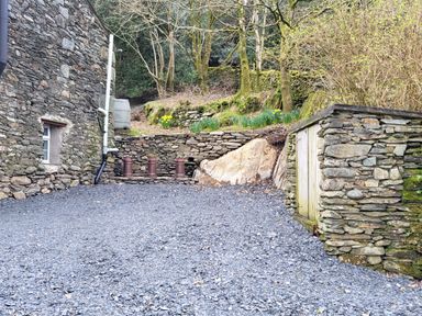 A gravel courtyard with stone walls and flower beds at High Kiln Bank Cottage in Seathwaite Duddon Valley