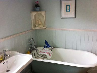 A bathroom with a bathtub and a sink and a small cabinet with a plant at Teds Place in Aylsham