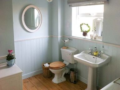 A bathroom with a toilet with wooden seat and a sink under a window at Teds Place in Aylsham