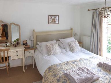 A bedroom with a double bed a dressing table with mirror and chair and a window with curtains at Teds Place in Aylsham