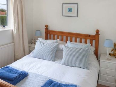 A bedroom with a wooden bed frame two blue striped pillows and two blue towels on the bed at Teds Place in Aylsham