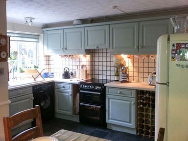 A kitchen with light blue cabinets black stove and a cream refrigerator at Teds Place in Aylsham