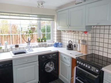 A kitchen with a sink under a window a black washing machine a stove and light blue cabinets at Teds Place in Aylsham
