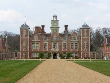 A large historic brick building with a central clock tower and multiple windows on a gravel pathway with grass on both sides at Teds Place in Aylsham