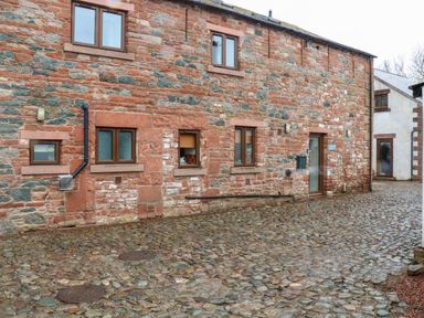 An exterior view of a stone building with multiple windows and a cobblestone ground at Blencathra Barn in Penrith