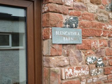 A close up of a stone wall with a metal sign reading Blencathra Barn next to a wooden framed window at Blencathra Barn in Penrith