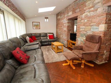 A living room with a grey leather sectional sofa and a brown reclining chair with ottoman near a stone wall with a TV at Blencathra Barn in Penrith