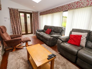 A living room with leather sofas a reclining chair coffee table and large windows with curtains at Blencathra Barn in Penrith