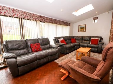 A living room with two gray sofas, a brown armchair with footrest, a wooden coffee table, and vertical blinds at Blencathra Barn in Penrith