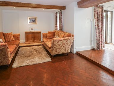 A living room with two sofas a wooden cabinet a rug on wooden flooring and floral curtains at Blencathra Barn in Penrith