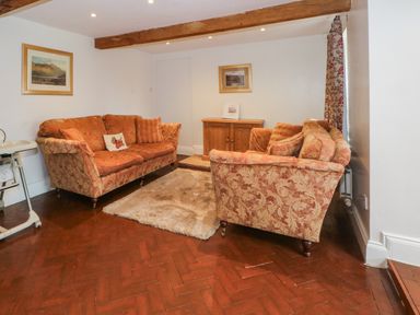 A sitting room with two patterned sofas a rug wooden cabinet and wooden beams at Blencathra Barn in Penrith