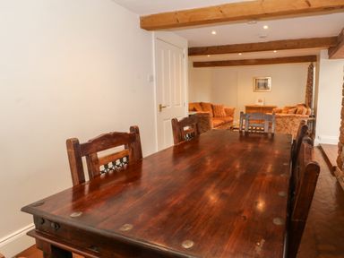 A dining table with chairs in a room with wooden beams and sofas in the background at Blencathra Barn in Penrith
