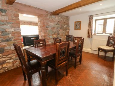 A dining room with a wooden table and chairs stone walls and a window with curtains at Blencathra Barn in Penrith
