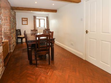 A dining room with a wooden table and chairs stone wall and a window with curtains at Blencathra Barn in Penrith