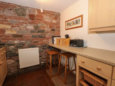 A kitchen corner with a stone wall wooden stools toaster and kitchen utensils at Blencathra Barn in Penrith