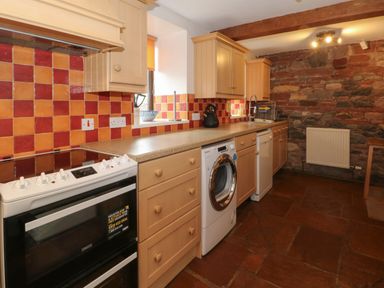 A kitchen with wooden cabinets a washing machine a dishwasher an oven and a tiled backsplash at Blencathra Barn in Penrith