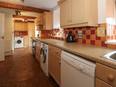 A kitchen with wooden cabinets red and orange tiled backsplash and appliances at Blencathra Barn in Penrith