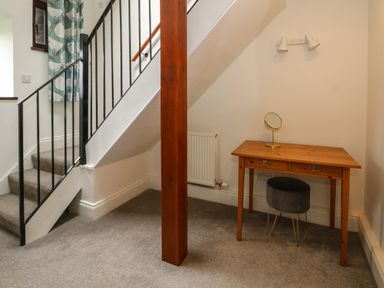 A small corner with a wooden desk, round mirror, stool, and carpeted stairs in a room at Blencathra Barn in Penrith