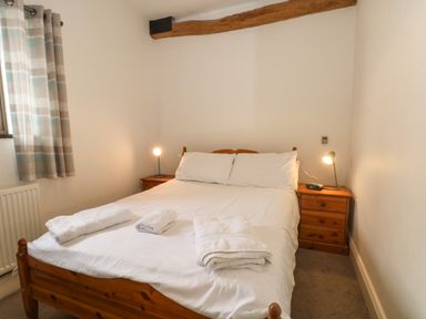A bedroom with a double bed white linens wooden bedside tables with lamps and folded towels on the bed at Blencathra Barn in Penrith