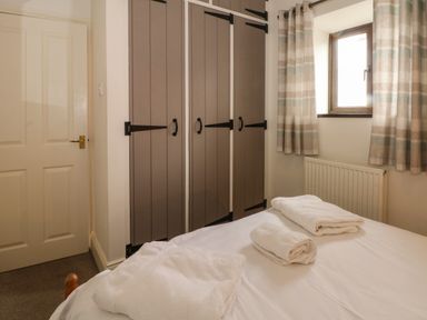 A bedroom with a bed, folded towels on the bed, a window with curtains, and a wardrobe with brown doors at Blencathra Barn in Penrith