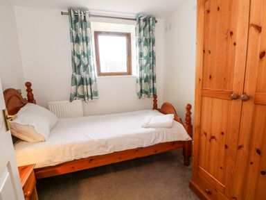 A small bedroom with a single wooden bed a window with patterned curtains and a wooden wardrobe at Blencathra Barn in Penrith