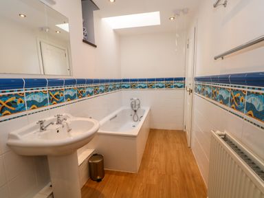 A bathroom with a sink a bathtub a radiator and tiled walls with blue fish patterns at Blencathra Barn in Penrith