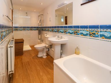 A bathroom with a bathtub a sink a toilet a shower and a wicker laundry basket at Blencathra Barn in Penrith