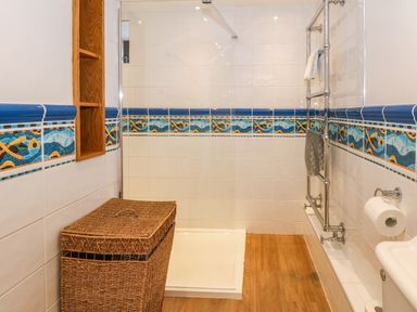 A bathroom with a wicker laundry basket a walk-in shower a chrome towel rack and fish-patterned tiles at Blencathra Barn in Penrith