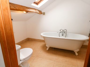 A bathroom with a toilet and a freestanding clawfoot bathtub under a wooden beam and skylight at Blencathra Barn in Penrith