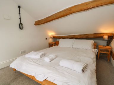 A bedroom with a double bed white linens wooden beams and bedside tables with lamps at Blencathra Barn in Penrith