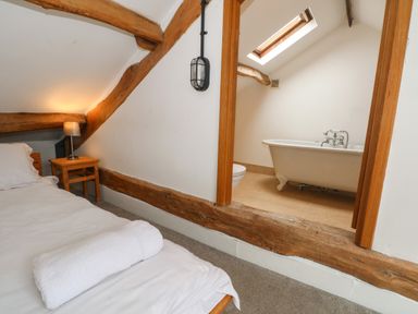 A bedroom with a bed and side table with lamp next to an open doorway showing a bathroom with a bathtub at Blencathra Barn in Penrith