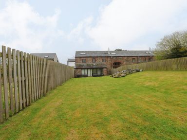 A green lawn enclosed by wooden fences with a stone house in the background at Blencathra Barn in Penrith