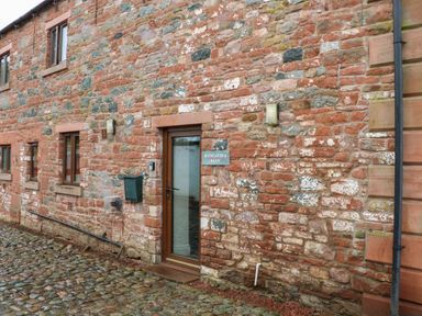 A stone exterior wall of a building with windows a glass door and a mailbox at Blencathra Barn in Penrith
