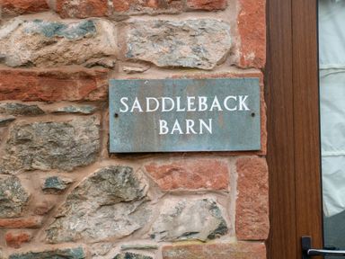 A sign reading Saddleback Barn on a stone wall next to a wooden door at Saddleback Barn in Newton Reigny near Penrith